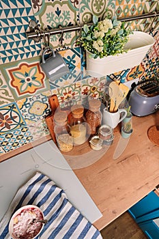 Cozy home style modern kitchen with colorful patchwork tiles, spice jars, glass jars with cereals and other kitchen accessories