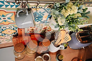 Cozy home style modern kitchen with colorful patchwork tiles, spice jars, glass jars with cereals and other kitchen accessories