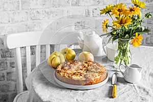 Cozy home tea party table - apple pie, bouquet of yellow flowers, teapot on a light table on a light background