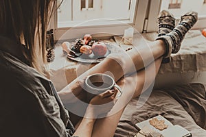 Cozy home. Woman with cup of hot drink sitting by the window.