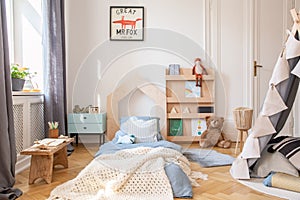 Cozy kids bedroom with blue bedding and warm blanket on the bed, real photo with mockup poster on the floor