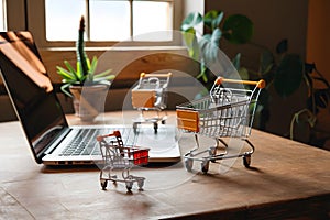 Cozy laptop setup with miniature shopping carts on wooden table, indoor setting.