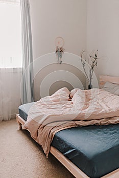 Cozy light and bright bedroom. Bed linen. White, beige, grey, blue. Wooden bed frame. Apartment living. Minimalist lifestyle.