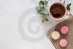 Cozy marble table. Eucalyptus leaves, cup of coffee, and French pastries macaroon. Top view, flat lay. Natural style