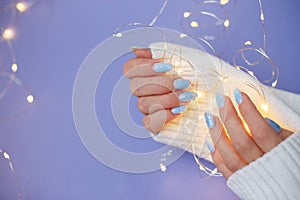 Cozy nails with winter manicure with snowflakes and lights on purple background