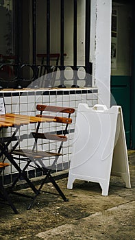 Cozy outdoor cafe with wooden table, metal railing, tiled section, and white signboard