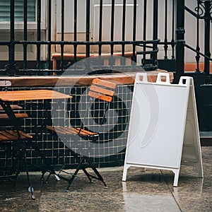 Cozy outdoor cafe with wooden table, metal railing, tiled section, and white signboard