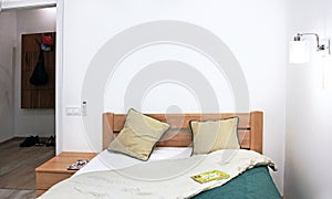 Cozy pan-bedroom interior with a green bedspread, two pillows, a luminous sconce, a book on the bedspread with a door to the