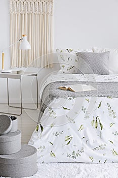 A cozy pastel bedroom interior with a bed dressed in green plants on white linen and cushions. Warm gray wool blanket on the bed.