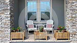 A cozy peaceful front porch of a house with adirondack chairs and flower planters