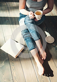 Cozy photo of young woman with cup of tea sitting on the floor