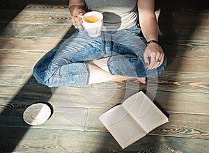 Cozy photo of young woman with cup of tea sitting on the floor