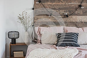 Cozy, pink bedroom interior for a girl with lights hanging on a wooden bedhead