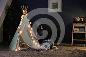 Cozy play tent for kids with glowing garland in room interior