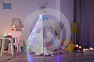 Cozy play tent for kids with glowing garland in room interior