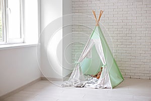 Cozy play tent for kids near white brick wall indoors