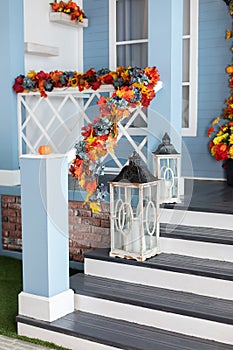 Cozy porch of the house with wooden lanterns in fall time. Halloween design home with yellow fall leaves and lamps