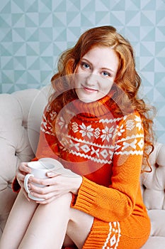 Cozy portrait of woman in warm sweater on the bed with cup of t