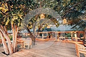 Cozy romantic outdoor tables and chairs in hotel resort bar. Dining on wooden deck, candles lights with trees