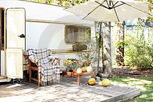 Cozy RV house porch with armchair with plaid and table. Campsite in garden. Interior yard campsite with flowers and pumpkins.