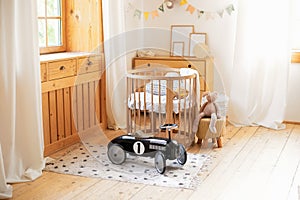 Cozy Scandinavian lights baby room: wooden crib with bedding and plush toys. Retro style child toy racing car in children room. Mo