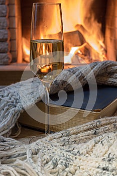 Cozy scene before fireplace with a glass of wine, a book, wool scarf