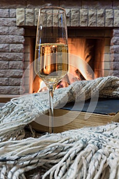 Cozy scene before fireplace with glass of wine, book and wool warm scarf