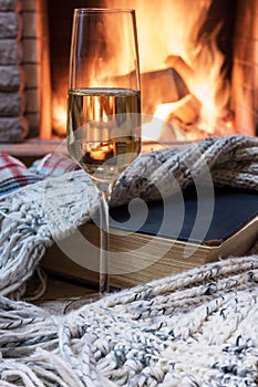 Cozy scene before fireplace with glass of wine, book and wool warm scarf