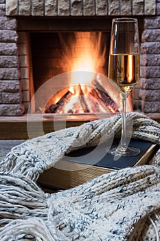 Cozy scene before fireplace with glass of wine, book and wool warm scarf