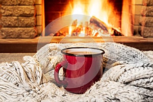 Cozy scene near fireplace with a Red enameled mug with hot tea and cozy warm scarf.