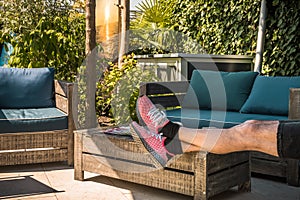 Cozy shady seating area with wooden furniture, a man puts his legs on the table to relax