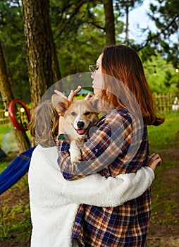 Cozy sisters holding their smiling welsh corgi dog