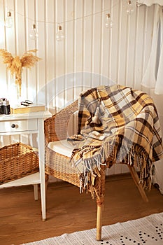 Cozy Skandinavian interior home with wicker rattan armchair and plaid. Rattan chair and wooden table with book in bedroom. Rustic