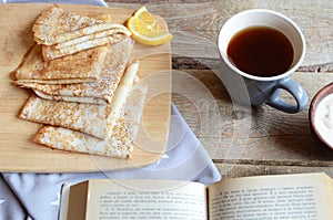 Cozy snack with Russian style pancakes and book during Maslenitsa Old wooden background