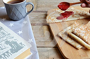 Cozy snack with Russian style pancakes and book during Maslenitsa Old wooden background