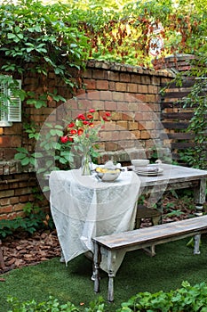 Cozy space in patio or balcony. Terrace outdoor with brick wall and plants, table and wooden bench. Garden in summer with patio,