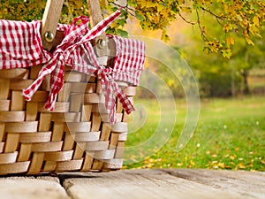 A cozy straw picnic basket on a wooden table against the backdrop of a picturesque autumn nature. Picnic, rest, family traditions