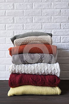 Cozy sweaters in autumn colors on brown wooden background.
