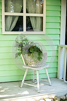 Cozy terrace with chair and basket with flowers. Decorations in summer patio for relax. Stylish fall decor on front porch home.  E