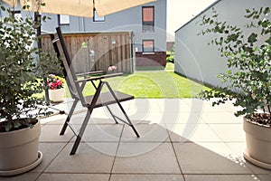 Cozy terrace with chairs under sun umbrella and green plants in sunny day