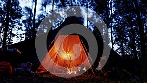 Cozy tipi with oil lamps and camp fire in a dark forest