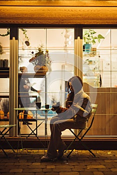 Cozy vertical photo of a female dog-owner with her little friend - york terrier, sitting on a terrace near the cafe in the evening