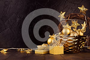 Cozy warm dark Christmas background with glowing golden stars lights, wreath, balls, gift box, ribbons in modern black interior.