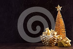 Cozy warm dark christmas background with golden star, christmas tree, balls, gift box, ribbons in modern black interior on brown.