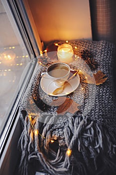 Cozy winter or autumn morning at home. Hot coffee with gold metallic spoon, warm blanket, garland and candle lights