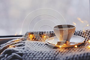 Cozy winter or autumn morning at home. Hot coffee with gold metallic spoon, warm blanket, garland and candle lights