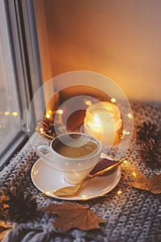 Cozy winter or autumn morning at home. Hot coffee with gold metallic spoon, warm blanket, garland and candle lights