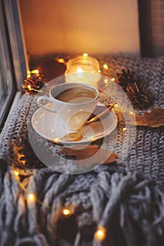 Cozy winter or autumn morning at home. Hot coffee with gold metallic spoon, warm blanket, garland and candle lights