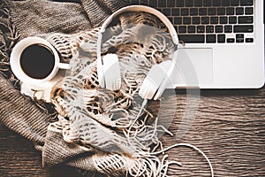 Cozy winter background, cup of hot coffee with marshmallow and headphone music, warm knitted sweater, work space laptop, photo