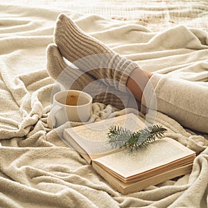 Cozy winter evening , warm woolen socks. Woman is lying feet up on white shaggy blanket and reading book. Cozy leisure scene